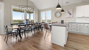 A spacious kitchen with white cabinets, a large island, and a dining area with chairs and a table. - Sunset State of Mind: Private Pool | Hot Tub | Elevator (Nags Head)