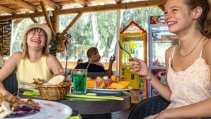Ein Essbereich im Freien mit Holzbalken, einem Tisch mit Speisen und Getränken sowie einem Greifautomaten im Hintergrund.