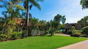 Un barrio residencial con césped cuidado, palmeras y una casa moderna de dos pisos.