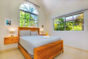 A bedroom with a large bed, two bedside tables, and a window with a view of greenery. - Hispaniola • Beach walk • Mega private pool • 3 BR (Sosúa)