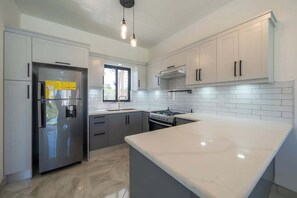 A modern kitchen with white cabinets, a stainless steel refrigerator, a gas stove, and a marble countertop. - Luxury Villa • Private Pool • 3BR (Sosúa)