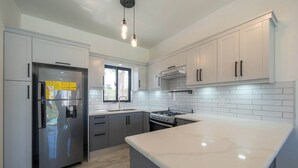 A modern kitchen with white cabinets, a stainless steel refrigerator, a gas stove, and a marble countertop. - Sun-Filled Villa • Sunlit Pool • Just Finished (Sosúa)