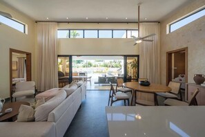 A spacious living area with a sofa, dining table, and chairs, large windows, and a view of the outdoors. - Elegance, Comfort, Location, 4BR Villa (Cabarete)