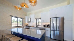 Una cocina moderna con una isla central, armarios blancos, electrodomésticos de acero inoxidable y un amplio ventanal.
