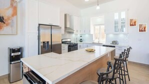 Une cuisine moderne dotée d’un grand îlot central, d’appareils électroménagers en acier inoxydable et de tabourets de bar.