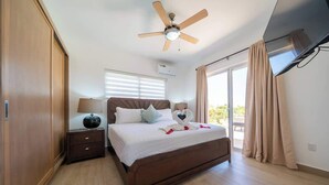 Une chambre à coucher avec un lit, une table de chevet, un ventilateur de plafond, une télévision et une fenêtre avec des rideaux.
