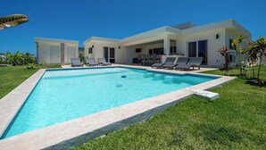 Une maison moderne dotée d’une piscine, de chaises longues et d’une pelouse bien entretenue.