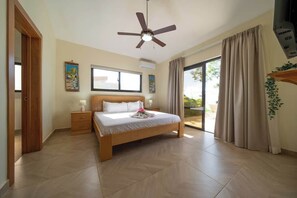Un dormitorio con cama, ventilador de techo, ventana y puerta corredera de vidrio.