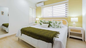 Une chambre à coucher avec un lit, des tables de chevet, un ventilateur de plafond et une fenêtre avec des stores.
