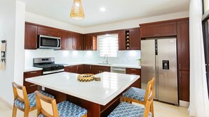 Une cuisine moderne avec des meubles en bois foncé, des appareils en acier inoxydable, un îlot central doté de chaises et un luminaire suspendu.