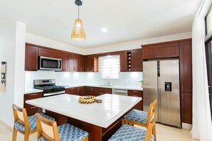 A modern kitchen with dark wood cabinets, stainless steel appliances, a central island with chairs, and a hanging light fixture. - Modern • Private • Relax (Sosúa)