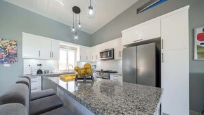 Una cocina moderna con armarios blancos, encimera de granito, electrodomésticos de acero inoxidable y un llamativo bol amarillo como elemento decorativo.