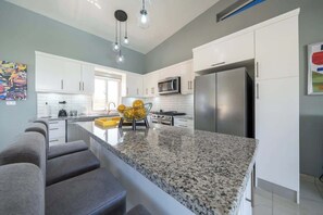 A modern kitchen with white cabinets, a granite countertop, stainless steel appliances, and a unique yellow bowl centerpiece. - Private Oasis — 3 King Suites — Brand New. (Sosúa)