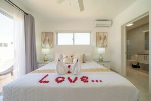 Ein Hotelzimmer mit einem Bett, zwei Nachttischen, einem Fenster und einem durch eine offene Tür einsehbaren Badezimmer.