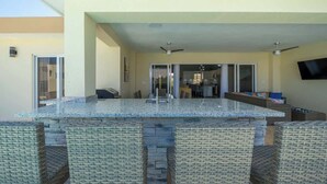 Un área de cocina al aire libre con barra, mobiliario de mimbre y ventiladores de techo.