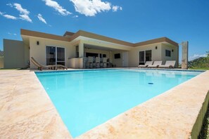 Ein modernes Haus mit Swimmingpool, überdachter Terrasse und blauem Himmel.