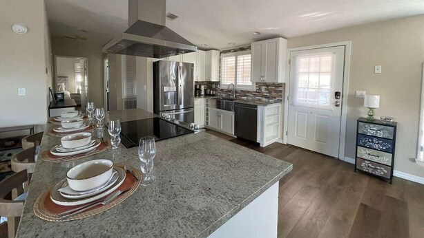 A modern kitchen with a central island, stainless steel appliances, and a dining area with a long table set for six. - Perfect Home in St. James City (Saint James City)