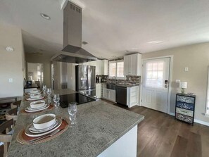 Cozinha moderna com ilha central, eletrodomésticos de aço inoxidável e área de jantar com mesa grande para seis pessoas.