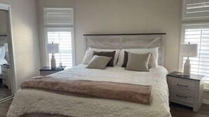 A bedroom with a bed, nightstands, a mirror, and windows with blinds. - Perfect Home in St. James City (Saint James City)