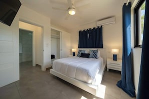 Ein Schlafzimmer mit einem Bett, Nachttischen, einem Deckenventilator und einem Fenster mit Vorhängen.