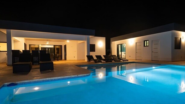 A swimming pool with lounge chairs, a covered patio, and a modern house exterior. - Location • Vibe • Style (Sosúa)