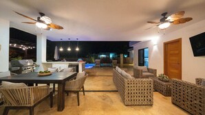 An outdoor patio area with a dining table, wicker furniture, ceiling fans, and a pool in the background. - Modern Villa · Pool, Jacuzzi & Pool Table · Sosúa (Sosúa)