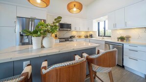 A modern kitchen with white cabinets, a large island, bar stools, and hanging wicker pendant lights. - Modern Villa · Pool, Jacuzzi & Pool Table · Sosúa (Sosúa)