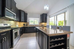 Eine moderne Küche mit dunklen Schränken, einer Granitabdeckung, Edelstahlgeräten und einem großen Fenster mit Blick auf Grünflächen.