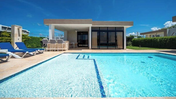 A modern pool area with lounge chairs and a building with large windows. - Modern 2BR Villa · Private Pool · Casa Linda (Sosúa)