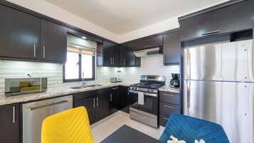 A modern kitchen with dark cabinets, stainless steel appliances, and a yellow and blue chair.