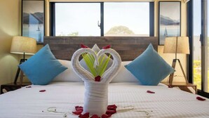 A bed with a white bedspread, two blue pillows, a vase with a floral arrangement, and a window with a view of a bridge and mountains. - Modern 2BR Villa · Private Pool · Casa Linda (Sosúa)