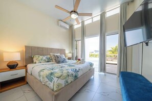 Une chambre à coucher comprenant un lit, une table de chevet, un ventilateur de plafond, une télévision et de grandes fenêtres.