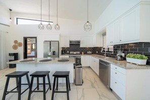 Una cocina moderna con una isla central, taburetes de bar, lámparas colgantes y armarios blancos.