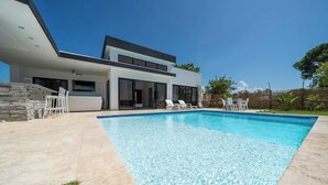 Ein modernes Haus mit Schwimmbad, Sitzgelegenheit im Freien und einer Steinmauer.