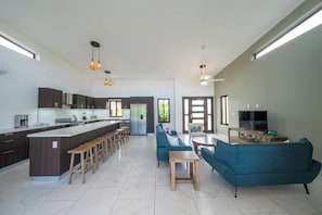 A modern kitchen with a central island, bar stools, a dining area with a sofa and table, and a TV in a living room. - New • All King • A/C in Living Room • Privacy (Sosúa)