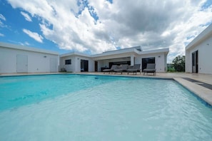 A swimming pool with lounge chairs, a covered patio, and a modern building with large windows. - New • All King • A/C in Living Room • Privacy (Sosúa)