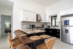 A modern kitchen with white cabinets, a stainless steel refrigerator, and a dining area with wicker chairs. - Soaring Pool Villa  •  Detached Pool Casita (Sosúa)