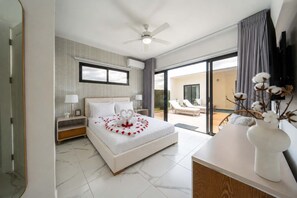 A modern bedroom with a large bed, a ceiling fan, a view to the outside, and a white console table with a vase. - Soaring Pool Villa  •  Detached Pool Casita (Sosúa)