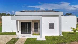 Una casa moderna de un solo piso con techo plano, una entrada central con puerta negra y un ventanal pequeño a la derecha.
