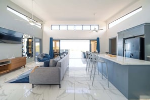 Una cocina moderna con barra, una mesa de comedor grande y un sofá en un amplio salón con televisor y ventiladores de techo.