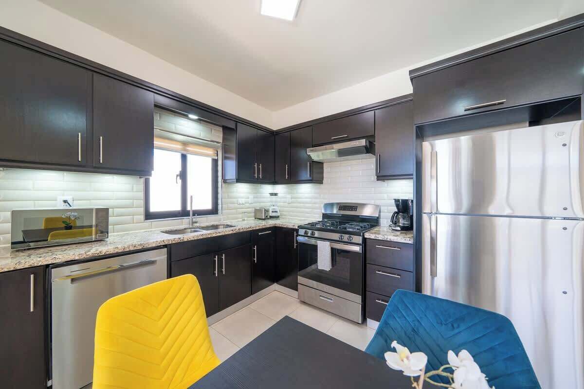 A modern kitchen with dark cabinets, stainless steel appliances, and a yellow and blue chair.