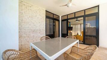 A dining area with a table and wicker chairs, a ceiling fan, and a brick wall.