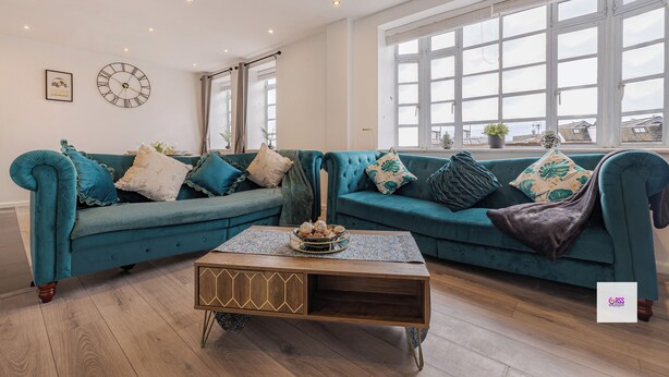 A teal sofa set with a wooden coffee table, a wall clock, and a large window with a view. - BRIGHTON CENTRAL TRENDY LONGSTAY, WALK TO BEACH (Brighton and Hove)