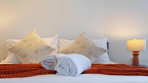 A neatly made bed with a rolled white towel, two pillows with floral patterns, and two bedside lamps on either side. - BRIGHTON CENTRAL TRENDY LONGSTAY, WALK TO BEACH (Brighton and Hove)