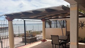 Eine überdachte Terrasse im Freien mit Tisch und Stühlen, einem gemusterten Boden und Blick aufs Meer.