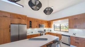 A modern kitchen with wooden cabinets, stainless steel appliances, a central island with bar stools, and pendant lighting.