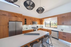 A modern kitchen with wooden cabinets, stainless steel appliances, a central island with bar stools, and pendant lighting. - 4 king suites • Mega large • Guest house (Sosúa)