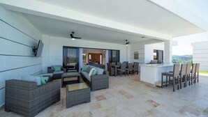 A spacious outdoor living area with wicker furniture, a bar, and a view of the landscape.