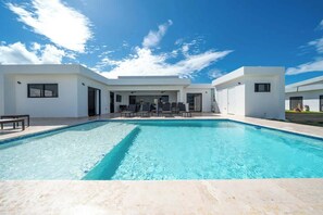 Ein moderner Poolbereich mit klarem, blauem Pool, weißen Wänden und einer überdachten Lounge-Ecke.