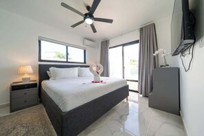 Ein Schlafzimmer mit Bett, Deckenventilator, Fernseher, Nachttisch, Schreibtisch, Stuhl und Fenster.